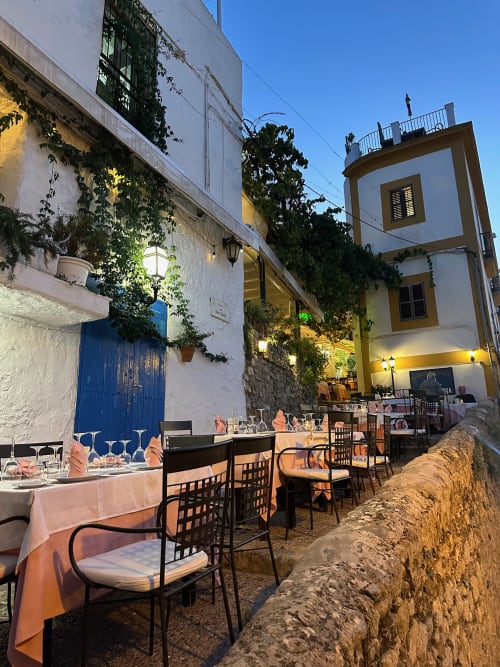 Outdoor dining terrace at Hotel La Ventana, Ibiza, with whitewashed buildings, ivy-covered walls, and elegant table settings