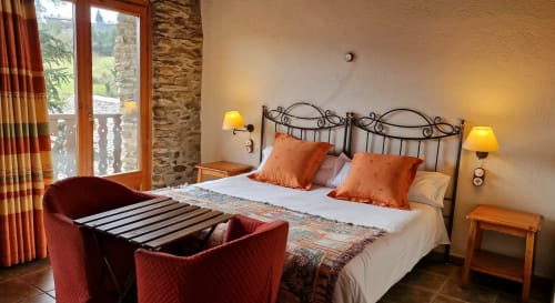 Habitación doble de lujo en Hotel Mas D'En Roqueta con cama de hierro ornamentada, almohadas naranjas y vistas al balcón
