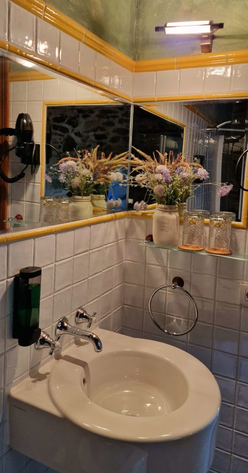 Lavabo moderno con espejo de marco amarillo, azulejos blancos y decoraciones de flores secas en Hotel Mas D'En Roqueta, España