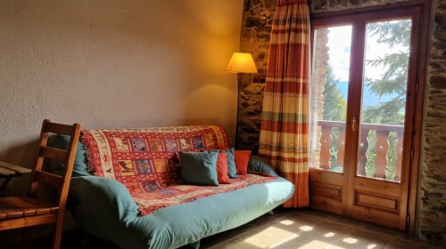 Luminosa habitación doble en Hotel Mas D'En Roqueta con sofá futón, cojines rojo estampado y puertas terraza