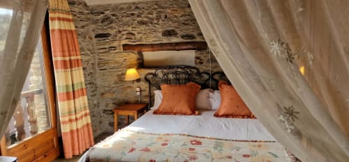 Dormitorio rústico de piedra en Hotel Mas D'En Roqueta con cama de hierro forjado, almohadas naranjas y cortinas translúcidas