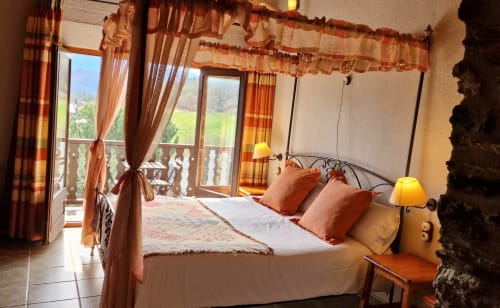 Lujoso dormitorio doble con cama con dosel, cortinas terracota y vistas panorámicas desde el balcón en Hotel Mas D'En Roqueta