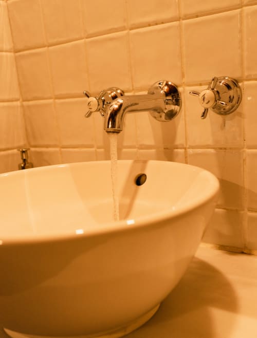 Elegante grifo bronce montado en pared con doble manija sobre lavabo circular en el baño del Hotel Mas D'En Roqueta