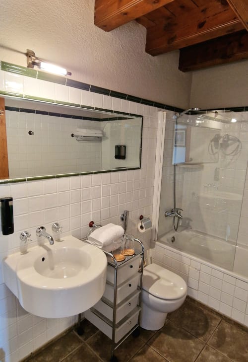 Baño moderno en la habitación Deluxe del Hotel Mas D'En Roqueta con azulejos blancos, lavabo redondo, inodoro y ducha con cristalería