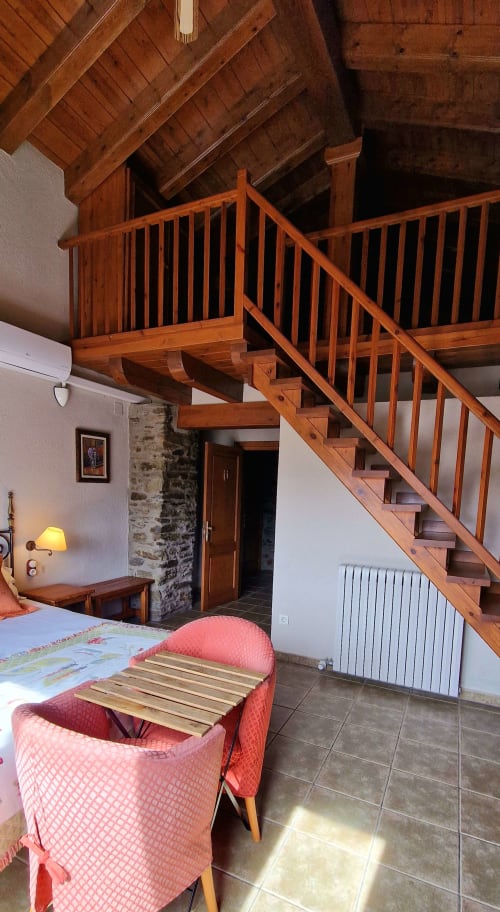 Habitación doble de lujo con escalera de madera, vigas vistas y silla rosa en Mas D'En Roqueta