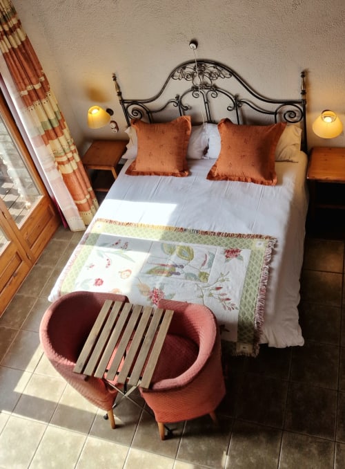 Elegante habitación doble en Hotel Mas D'En Roqueta con cama de hierro ornamental, almohadas color óxido y comodidades modernas en España