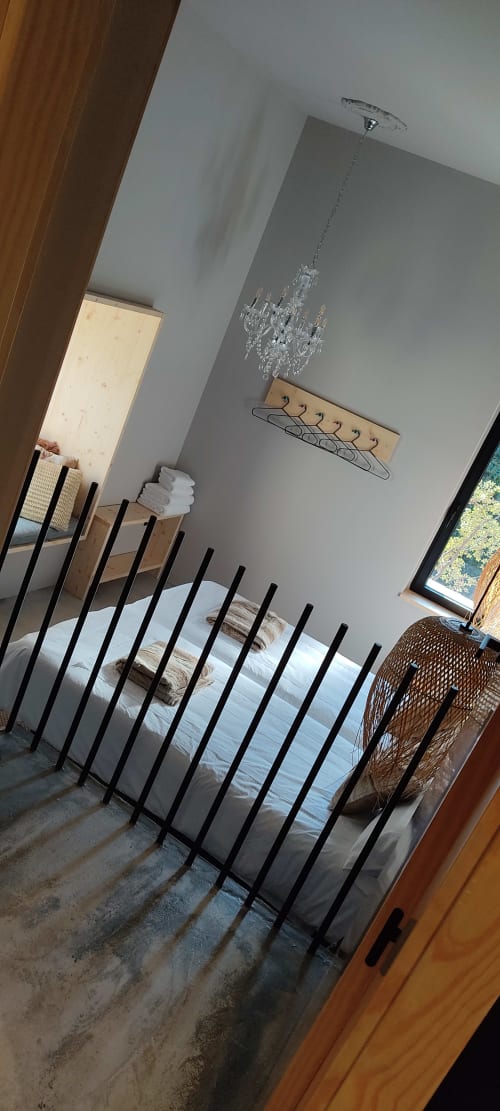 Habitación de cabaña en Hotel Mas D'En Roqueta con cama de estructura metálica negra, ropa de cama blanca, paredes grises y lámpara de cristal