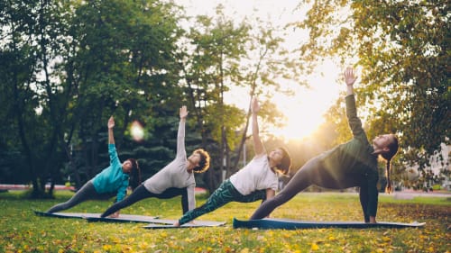 Cours de yoga en groupe dans le parc près du gîte La Ferme 1828 à Megève, France, avec arbres et lumière dorée du coucher de soleil
