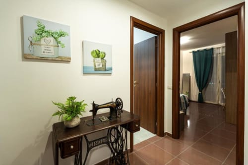 Grecale Room at Torre dei Venti BnB entrance with vintage sewing table, potted plants, wall art, and wood-framed doorways in