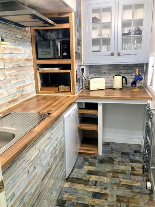 Modern kitchenette in Seashell Suite at Commodore hotel with wooden counters, white cabinets, microwave, kettle, and