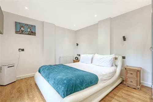 Spacious bedroom at Blackbrook Cottages The Stables with queen bed, turquoise throw, wooden nightstand, and white walls