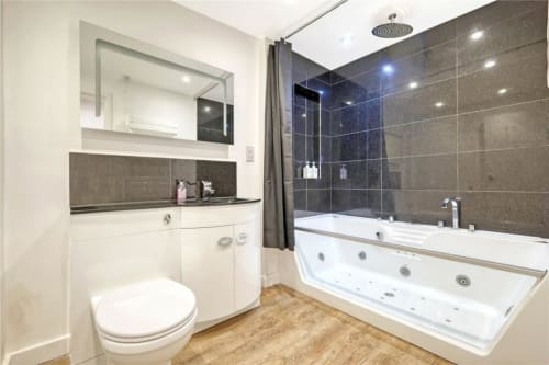 Modern bathroom in The Stables apartment at Blackbrook Cottages, Colchester, featuring white vanity, spa bath, and dark tiled