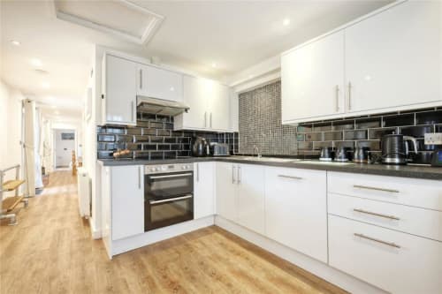 Modern white kitchen with black subway tile backsplash, dark countertops, stainless steel appliances, and wooden flooring at