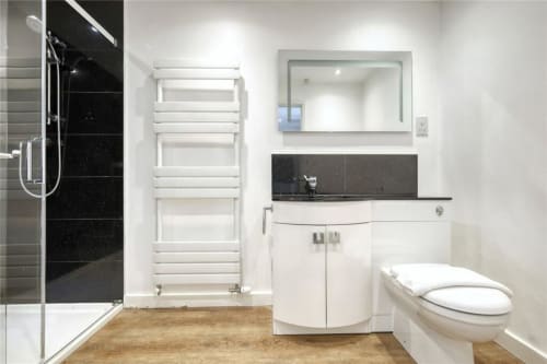 Modern bathroom at Blackbrook Cottages with white vanity, black countertop, mirror, heated towel rack, and walk-in shower