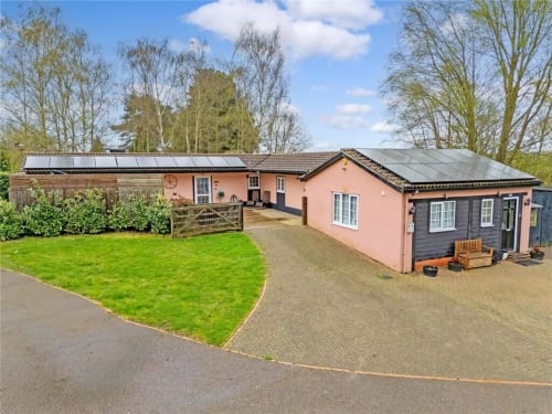 The Stables cottage at Blackbrook Cottages in Colchester with pink exterior, solar panels, paved courtyard, and manicured