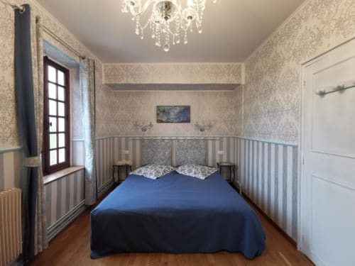 Chambre douillette au Coin des Artistes avec couvre-lit bleu, papier peint damassé, lustre ouvragé et vue sur la ville