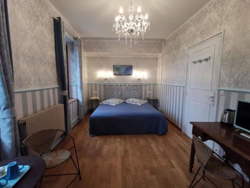Chambre élégante au Coin des Artistes avec lit bleu, lustre orné, papier peint rayé et mobilier d'époque