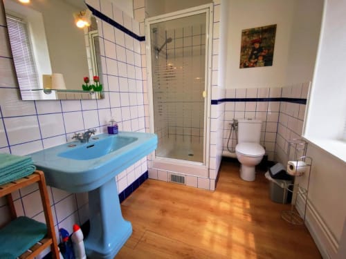 Salle de bains lumineuse au Coin des Artistes avec lavabo bleu, douche spacieuse, toilettes et parquet