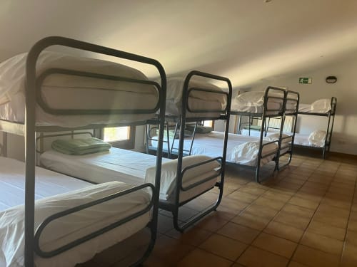 Multiple metal bunk beds with white linens in San Donato dormitory room at Posada de Ollo, Spain