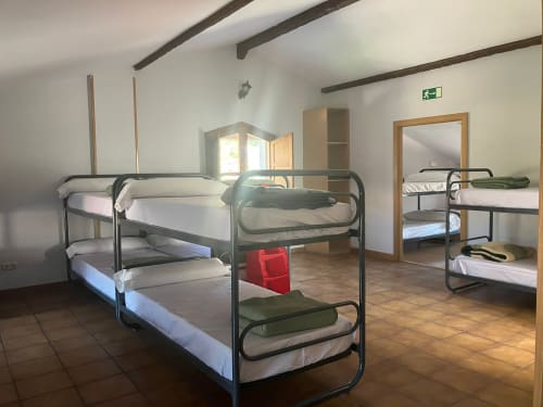 Dormitory room at Posada de Ollo with metal bunk beds, wooden beams, and shared bathroom facilities