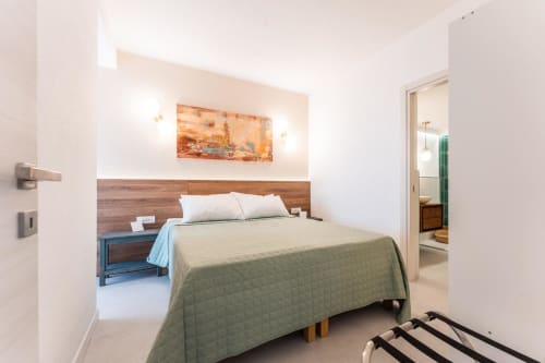 Camera da letto moderna con vista mare nell'appartamento eDomos Cagliari, testata in legno, copriletto trapuntato verde e bagno ensuite