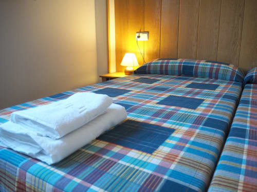 Cozy double bedroom at Posada de Ollo with plaid bedding, folded towels, and warm bedside lamp lighting