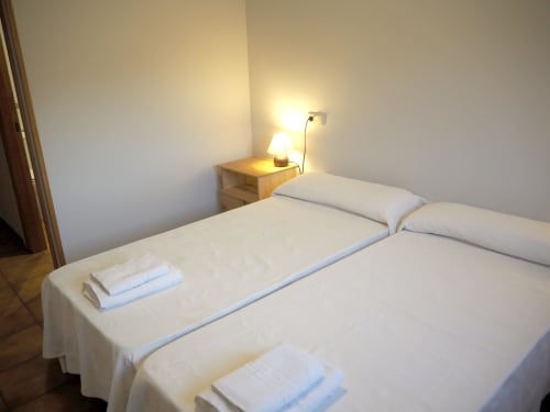 Clean double bedroom at Posada de Ollo with white bedding, wooden nightstand, and warm lamp lighting