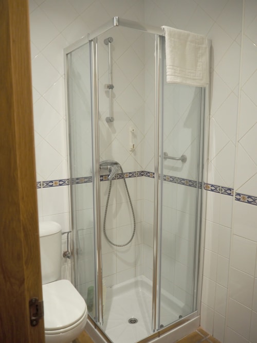Modern glass shower enclosure in Posada de Ollo hotel room with white tiles and decorative blue trim