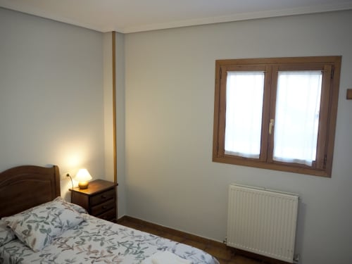 Bright bedroom at Posada de Ollo with wooden bed, nightstand lamp, and windows overlooking mountains in Spain