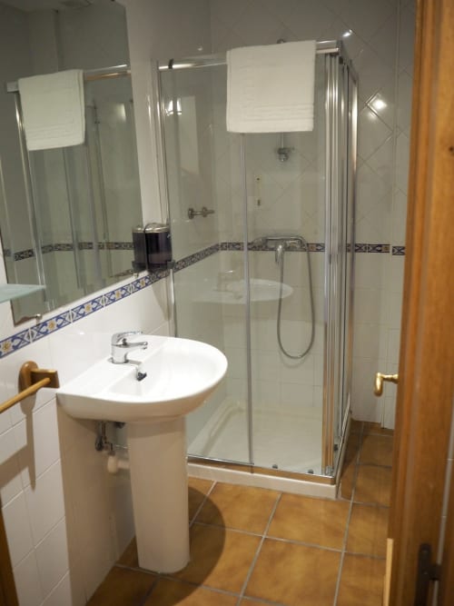 Modern bathroom at Posada de Ollo with shower enclosure, pedestal sink, and decorative tile border