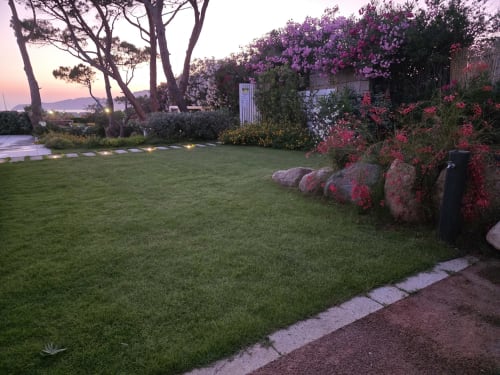 Twilight view of Villagì Luxury Villa garden in Cagliari with manicured lawn, blooming bougainvillea, mature trees, and sea