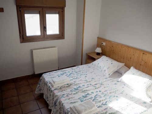 Bright bedroom at Posada de Ollo with two beds, wooden headboard, radiator, and window with mountain view