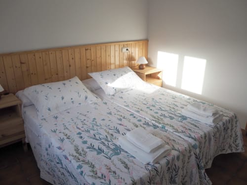 Bright double bedroom at Posada de Ollo with floral bedding, wooden headboard, and mountain views through windows