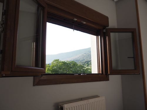 Open brown window at Posada de Ollo with mountain view and green trees in Beriáin, Spain
