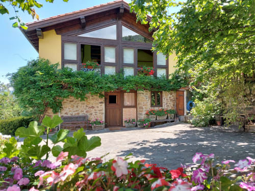 Rural apartment with stone base, wooden upper level, surrounded by lush gardens with colorful flowers at Los Picos De Redo,