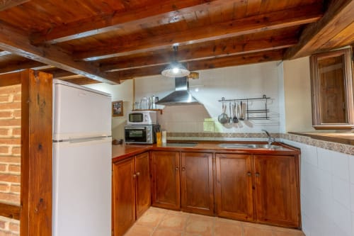 Rustic kitchen with wooden beams, red cabinetry, and white appliances at Los Picos De Redo rural apartment in Camaleño