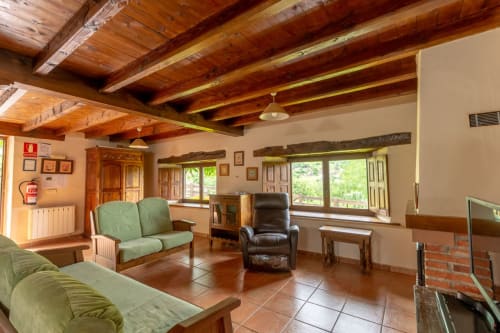 Rustic apartment living room at Los Picos De Redo with wooden beams, green sofas, and garden views in Camaleño