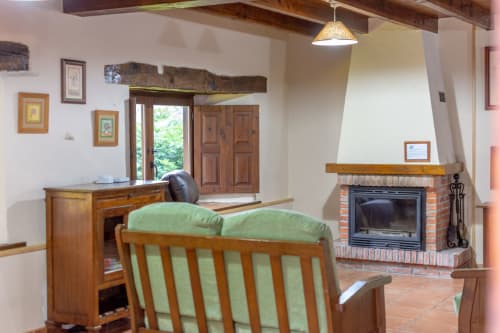 Rustic apartment living room with fireplace, wooden furniture, and green upholstered seating at Los Picos De Redo in Camaleño