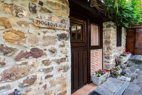 Mogrovejo apartment entrance at Los Picos De Redo with stone facade, wooden door, and garden flowers in Camaleño