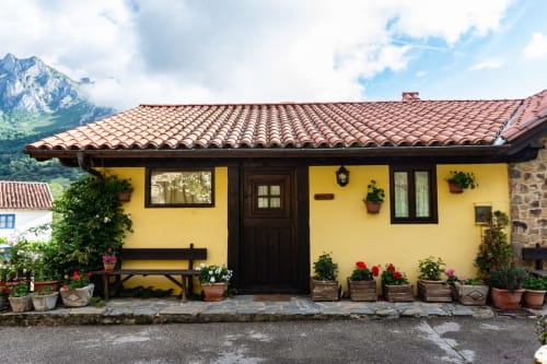 Apartamento rural amarillo brillante con tejado de barro, flores y vistas a la montaña en Camaleño, España