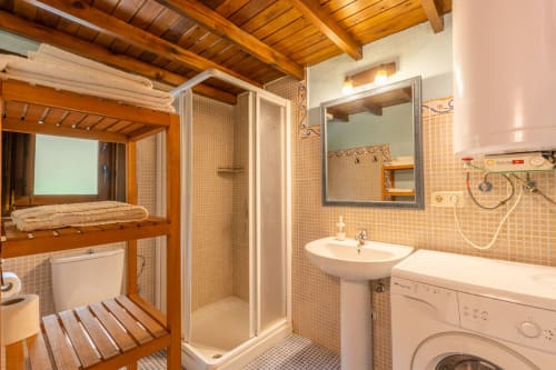 Baño con vigas de madera, azulejos naranjas, mampara de ducha, lavabo pedestal y lavadora en Los Picos de Redo rural