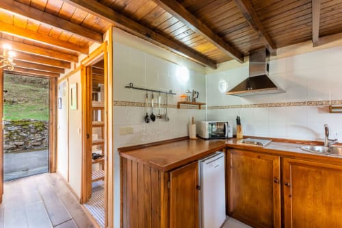 Cocina de madera con vigas vistas, barra de comedor, estufa y vistas al jardín del apartamento Los Picos De Redo, Camaleño