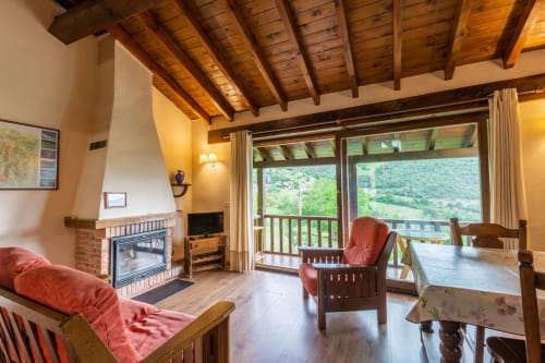 Sala de estar del apartamento Sebrango con chimenea, vigas de madera, vistas a las montañas a través de puertas de cristal y muebles rústicos