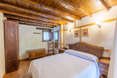 Dormitorio rústico en Apartamentos Los Picos De Redo con vigas de madera, cama queen y mobiliario tradicional en Camaleño, España