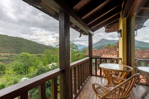Balcón del apartamento Sebrango con sillas de mimbre con vistas a los valles verdes y las montañas de Los Picos de Redo, Camaleño