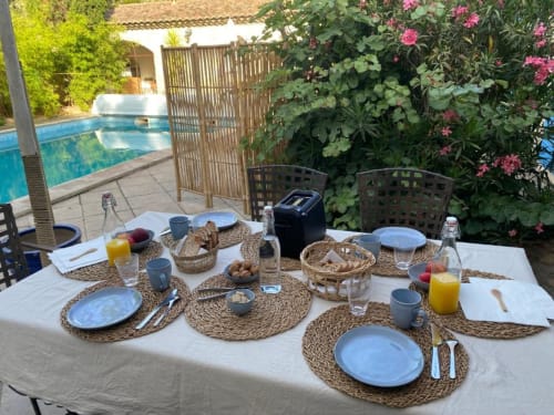 Espace repas extérieur au Patio aux Oiseaux avec assiettes bleues, jus frais et vue sur la piscine à La Ciotat
