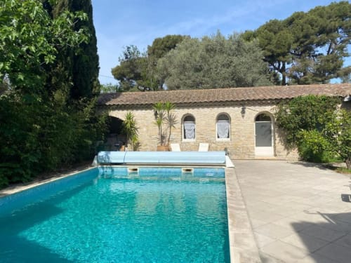 Piscine turquoise couverte et bâtiment en pierre aux fenêtres cintrées du Patio aux Oiseaux à La Ciotat
