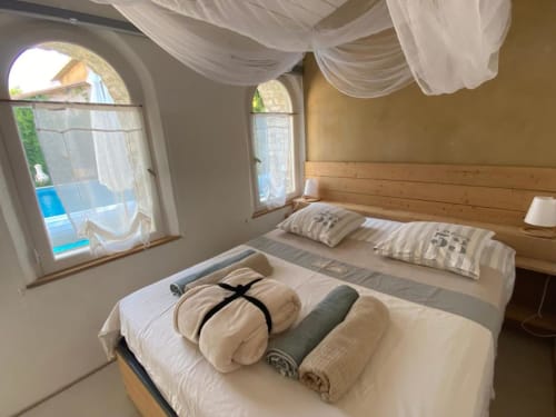 Chambre lumineuse au gîte Le Patio aux Oiseaux à La Ciotat avec lits jumeaux, tête de lit en bois, fenêtres cintrées et vue sur la piscine