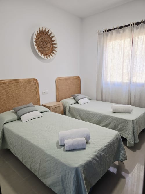 Dormitorio luminoso con dos camas individuales, cabeceras de ratán tejido y ropa blanca en el apartamento Ona vacaciones de la playa de Gandía