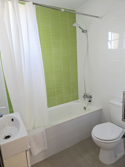 Baño moderno con azulejos verdes brillantes, cortina de ducha blanca, inodoro y lavamanos en apartamento de playa en Gandía